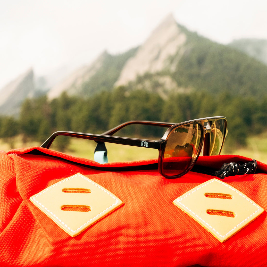 A pair of Howlin' Topo Edition sunglasses sit on a bright red Topo Designs backpack