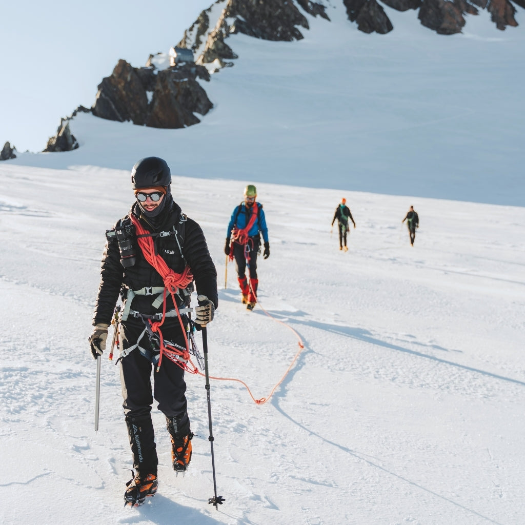 A group of mountaineers roped up together walk across a snowy plateau wearing VALLON Cat. 4 Heron Glacier sunglasses for maximum sun protection