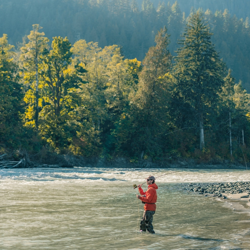 A man fishing on a river surrounded by pine trees wears VALLON polarized Freshwater Revivals sunglasses