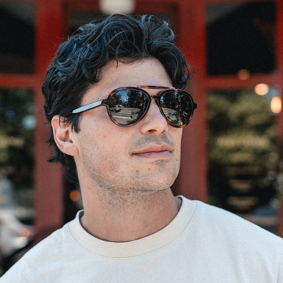 Man wears Elmore brow-bar aviator sunglasses with classic 80s style in front of a city grocery store