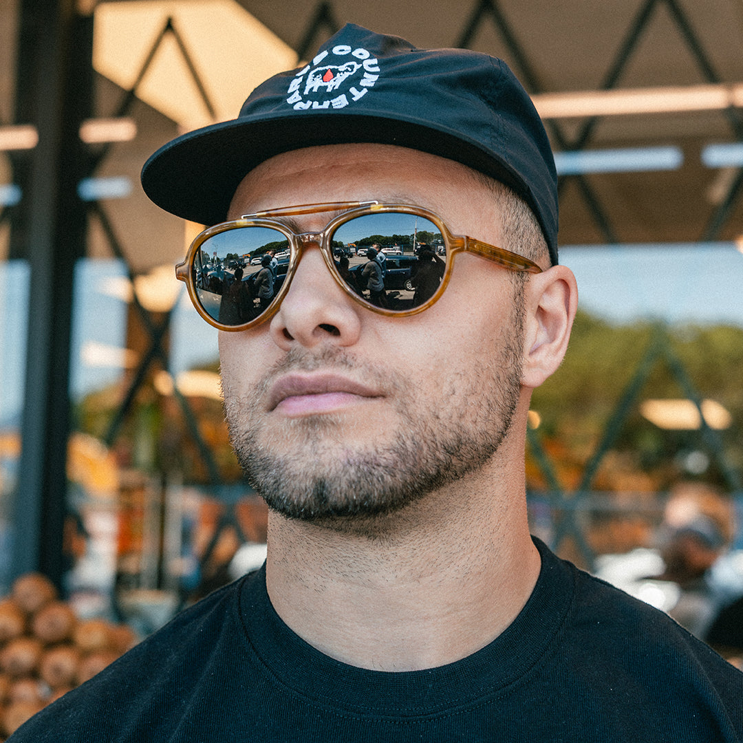 Man wears Elmore brow-bar aviator sunglasses with classic 80s style in front of a city grocery store