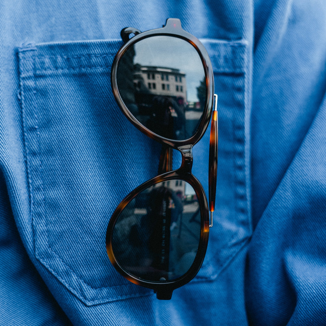 Elmore sunglasses from VALLON are aviator sunglasses with brow-bar design, V52 optics and sports versatility, shown hanging out of a blue shirt pocket