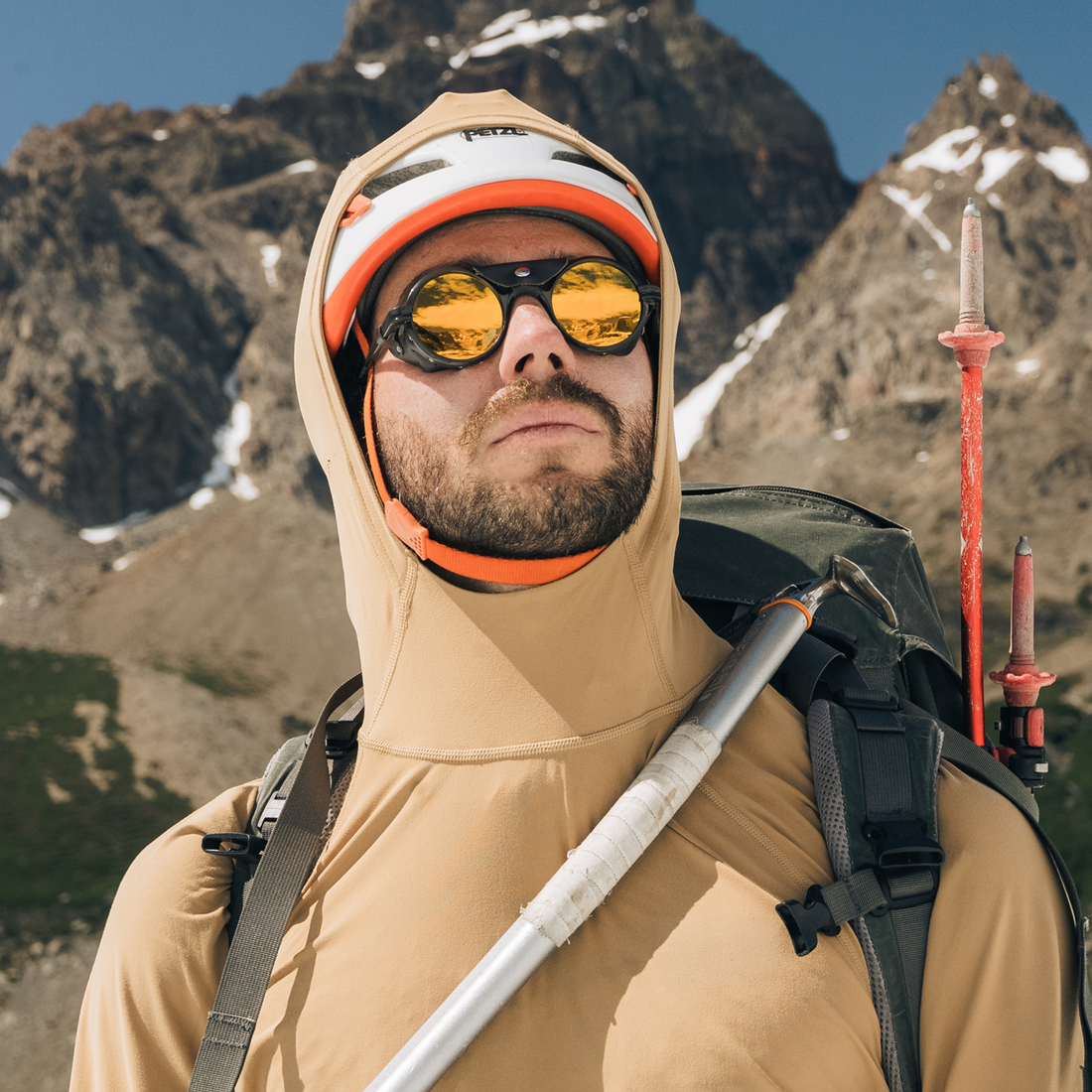 A man ready for climbing wears Brown-Yellow Heron Glacier glasses from VALLON for mountaineering, along with a white helmet, ice axe and backpack