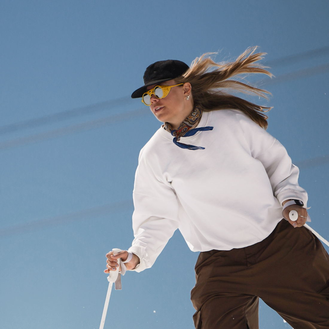 Woman wears Heron Glacier Yellow sunglasses from VALLON for skiing on a bluebird day