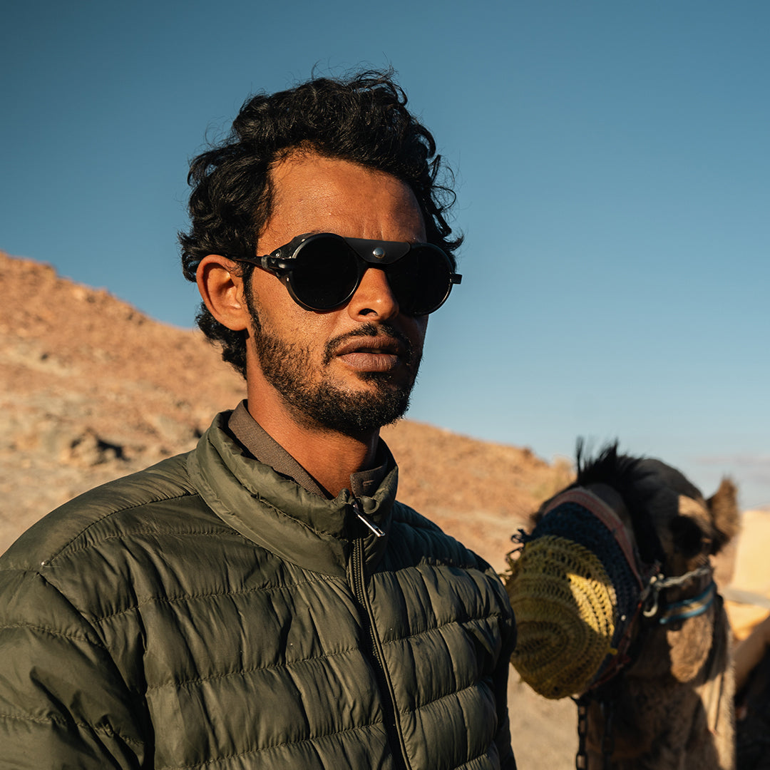Man wears Heron Desert sunglasses from VALLON for camel trekking in the desert