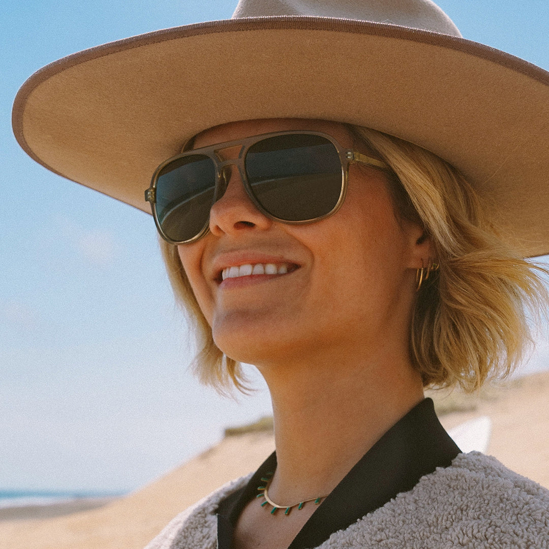Woman wears Howlin' sunglasses from VALLON in sage at the beach