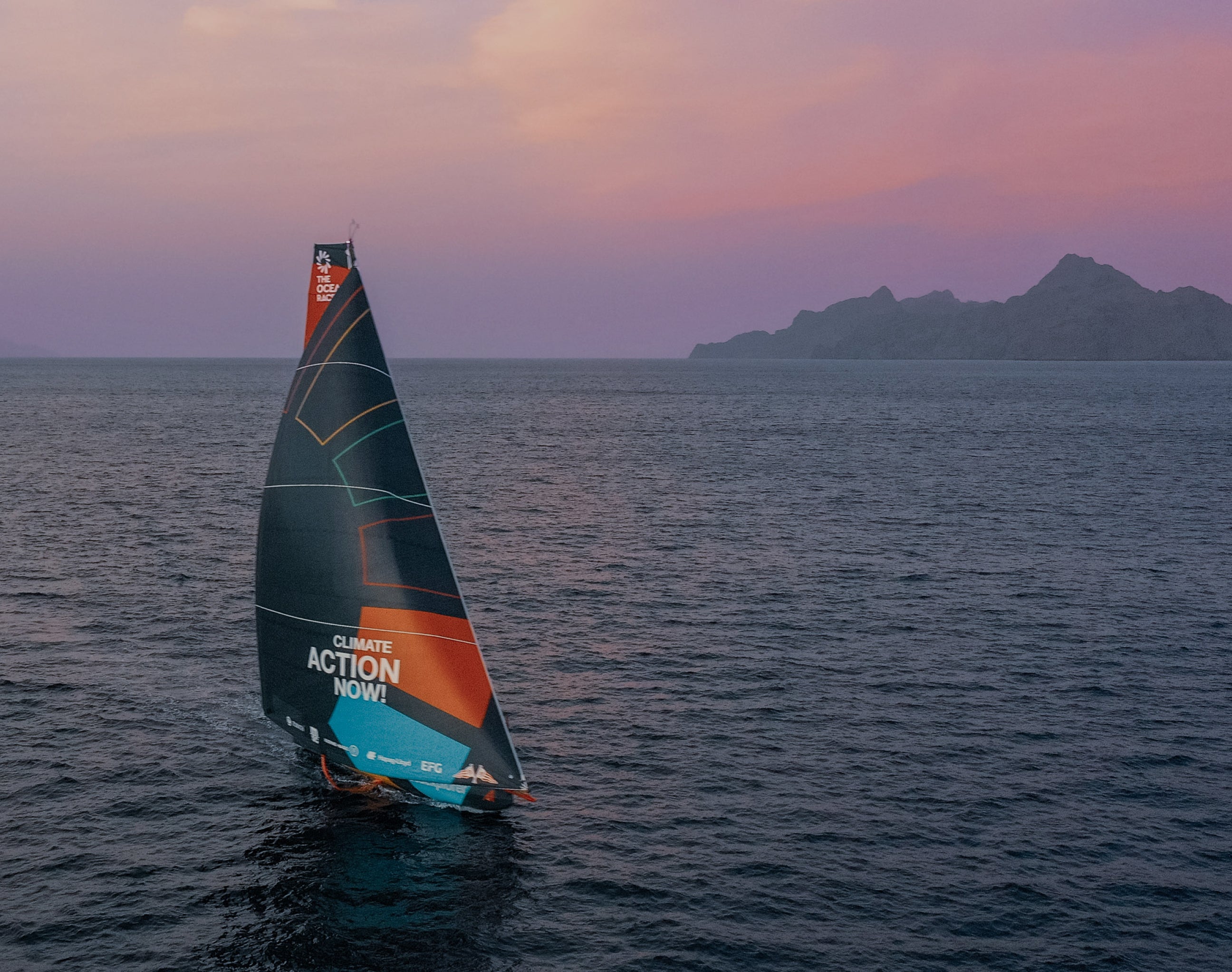 Malizia's sailing boat with 'Climate action now' sails at sunset on the open water