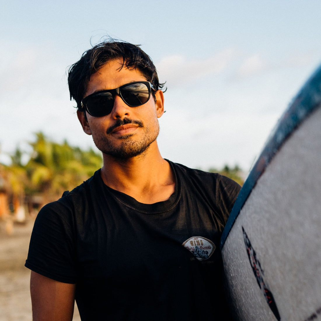 Man wears VALLON Wilburys acetate sunglasses with V52 lenses for surfing at the beach